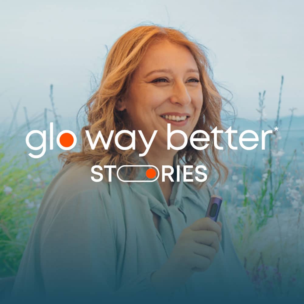 A woman with wavy blond hair smiles while holding a small device outdoors, with the text glo way better STORIES overlaid on the image.